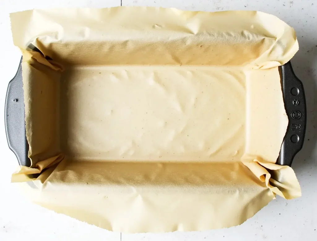 Empty loaf pan lined with parchment paper, ready for vegan banana bread batter.