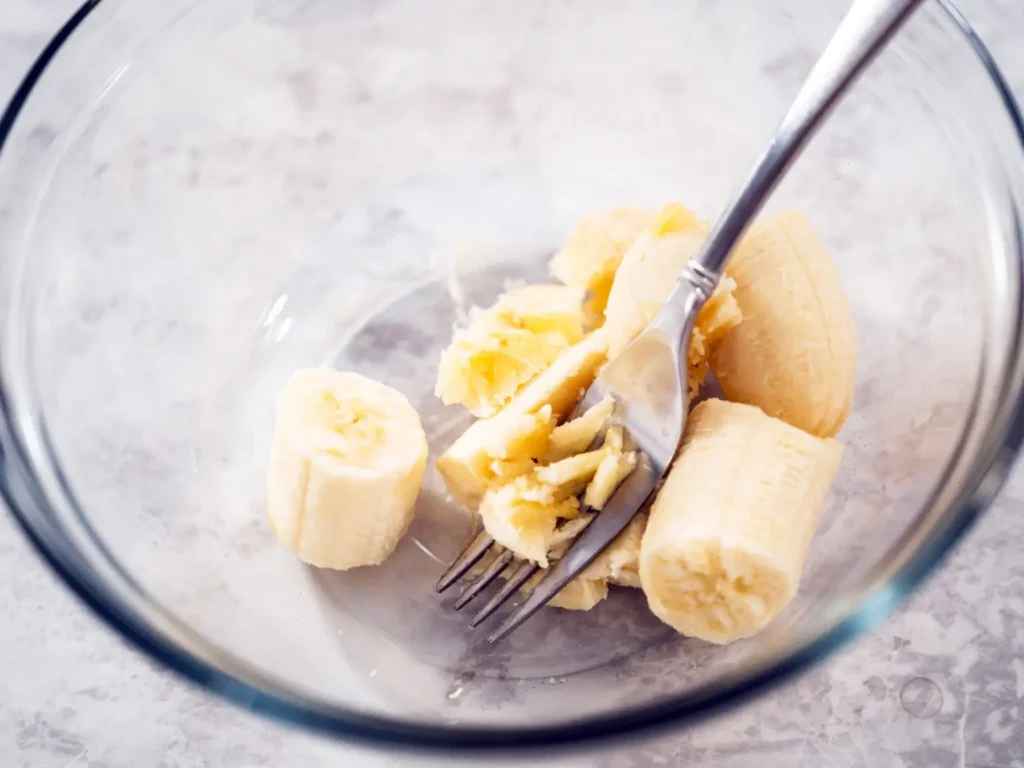 Partially mashed bananas in a glass bowl with a fork, ready to be mixed for vegan banana bread.